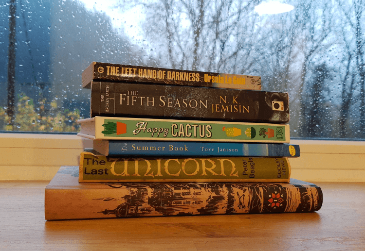 A stack of books sit on a windowsill.